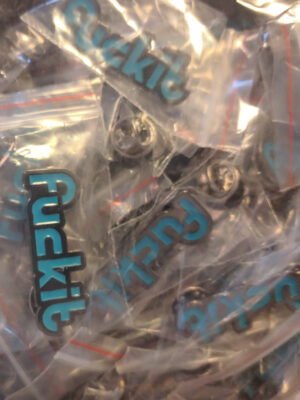 A punch of Funkit logo pins in tiny clear bags. The logo is turquoise, with a gray metal outline, and the n in funkit is turned sideways to look like it says fuckit.